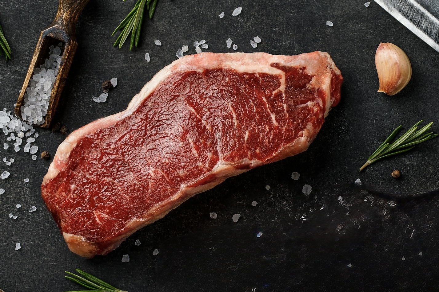 premium raw new york strip steak on dark stone surface, professional food photography, high-end, detailed meat texture